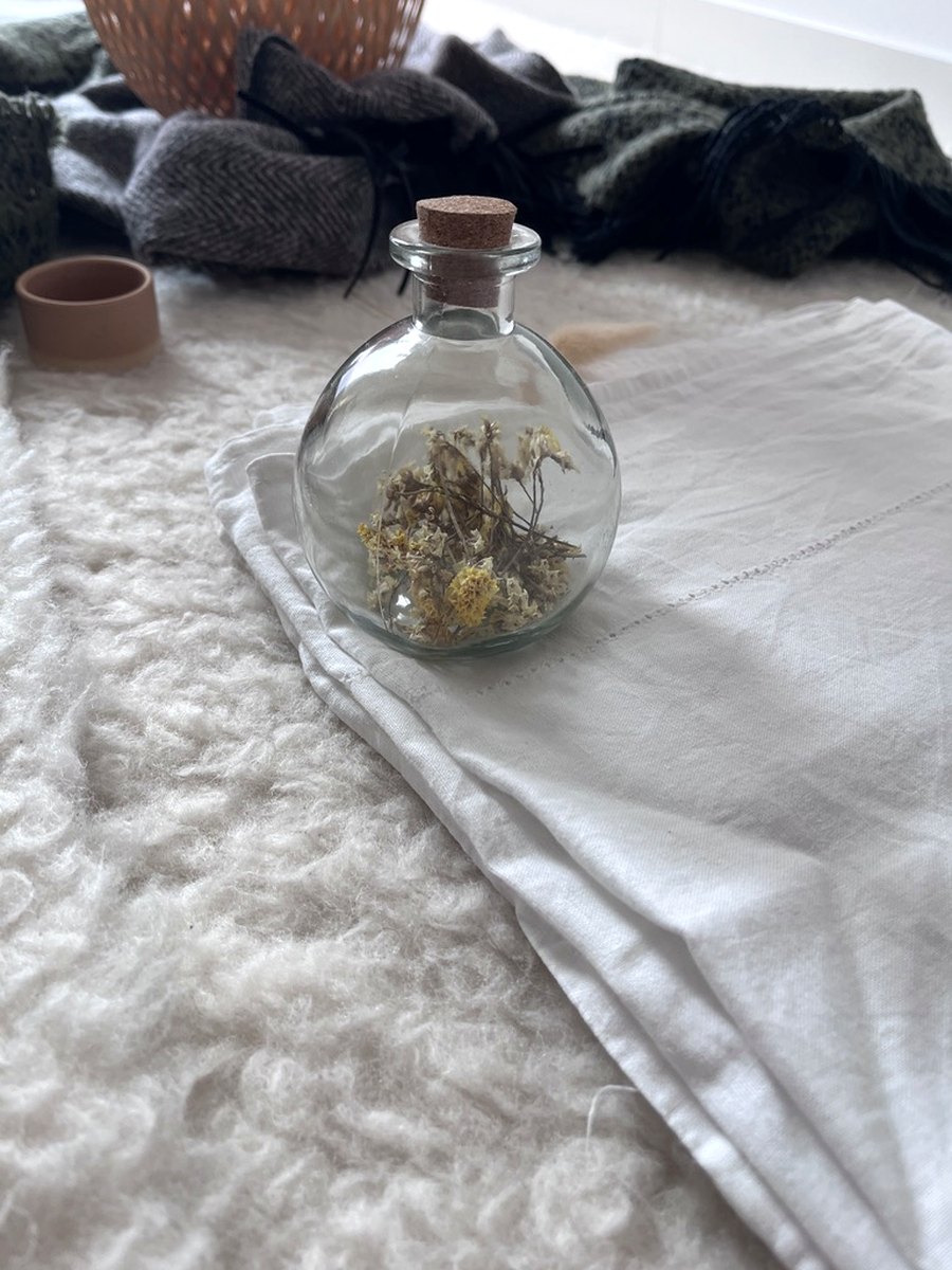 Glasflasche mit getrockneten Blüten auf einem Leinentuch